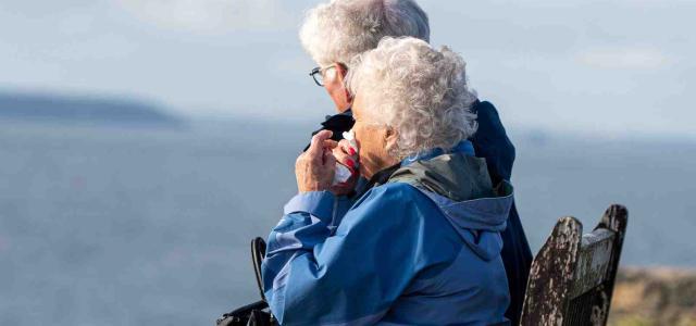 Two elderly people sitting on a bench looking at the sea